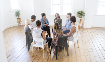Woman speaking in group therapy session Woman speaking in group therapy session. Members of support group sitting on chairs at entrance hall. Males and females are sharing ideas during group therapy.